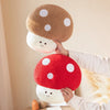 A hand is holding a large, round red mushroom plush toy with white polka dots and a smaller white mushroom below it.