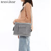 A person is wearing a grey Insular stroller organizer bag with a bottle holder on their shoulder.