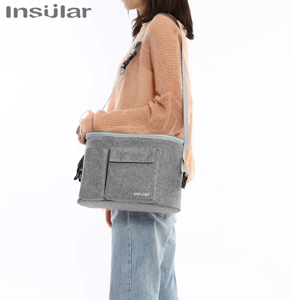 A person is wearing a grey Insular stroller organizer bag with a bottle holder on their shoulder.