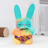 A bright turquoise and yellow monster plush toy with large blue bunny ears and a purple patterned belly.