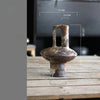 A vintage handcrafted ceramic vase with an elongated spout and a flared base, shown on a wooden surface.