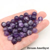 A handful of round purple amethyst beads is held in a person's hand.