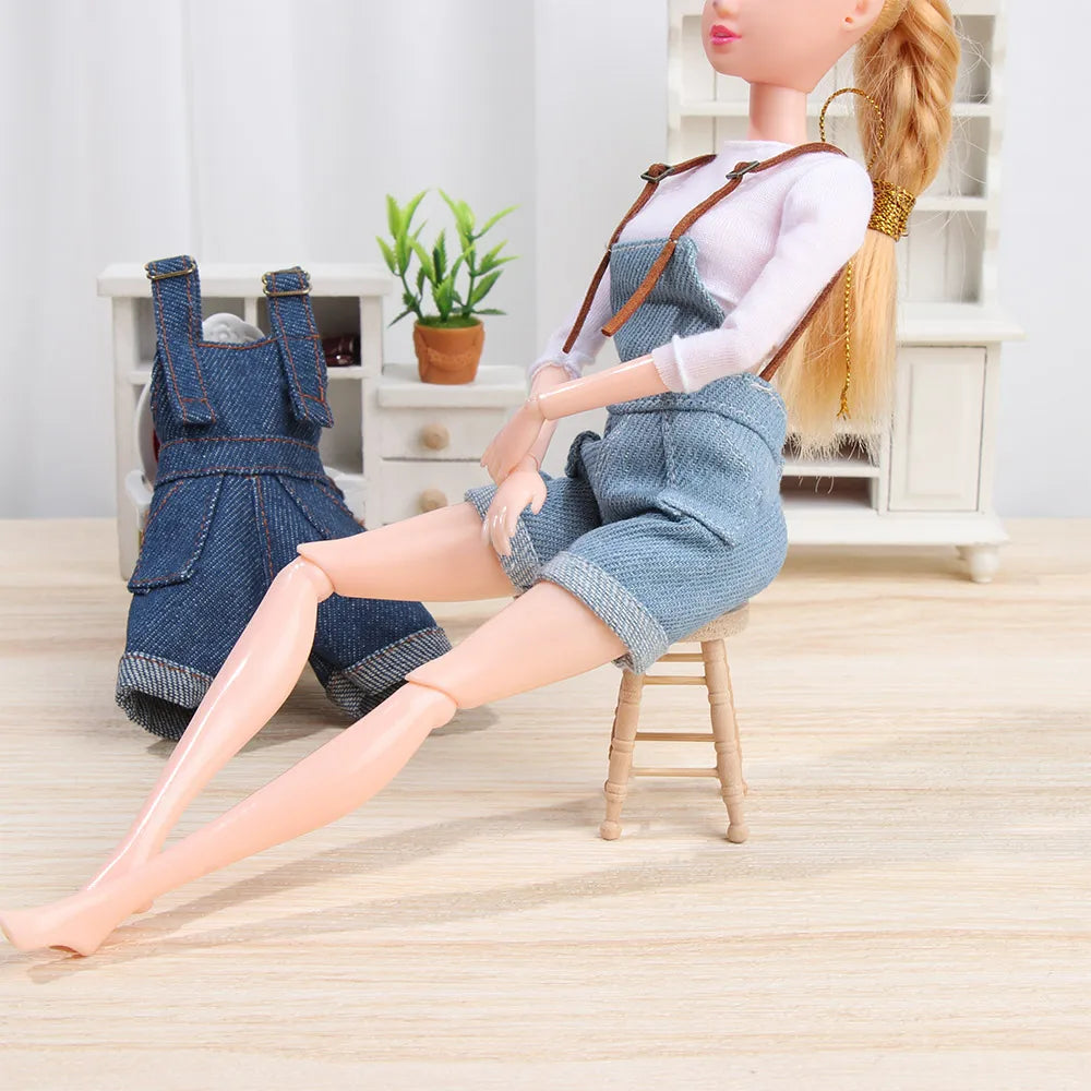 A mini doll wearing denim overalls and a light pink shirt sitting on a wooden stool.
