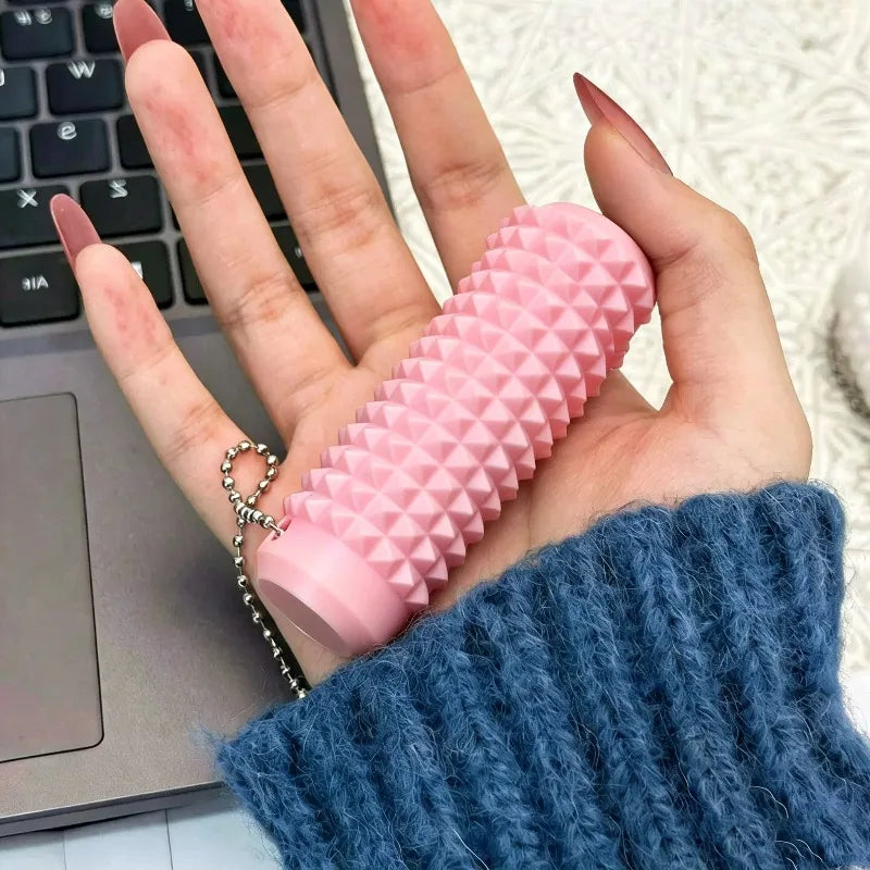 A hand holds a pink, textured fidget roller keychain against a blue knitted sleeve next to a laptop keyboard.