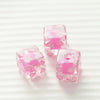 Two square pink resin beads with small floral designs are shown on a white background.