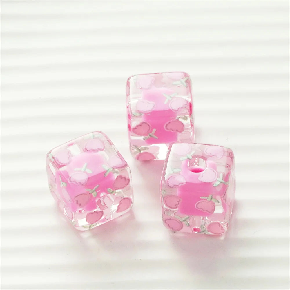 Two square pink resin beads with small floral designs are shown on a white background.