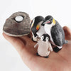 A hand holds a set of three penguin figures and a smooth stone for an animal life cycle learning kit.