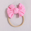 Pink fabric bow headband with a light beige elastic band on a white background.