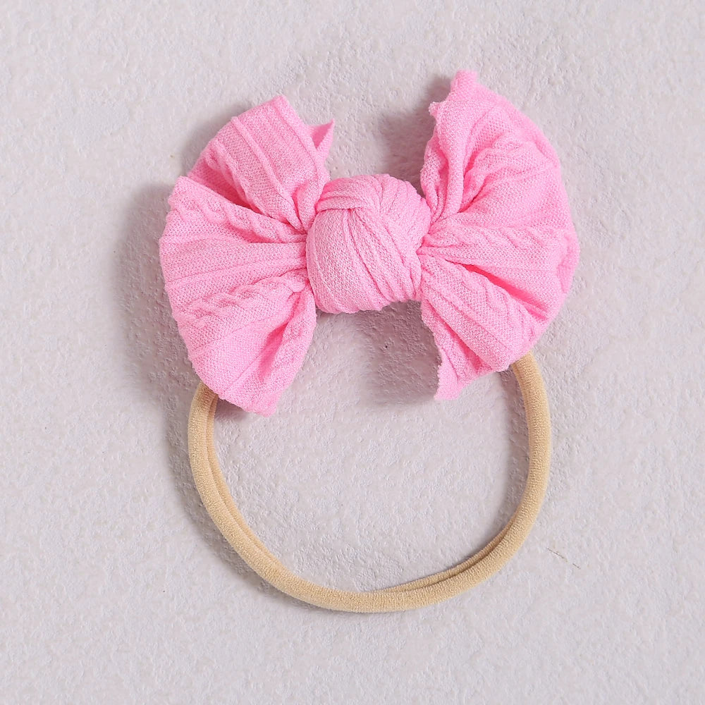 Pink fabric bow headband with a light beige elastic band on a white background.