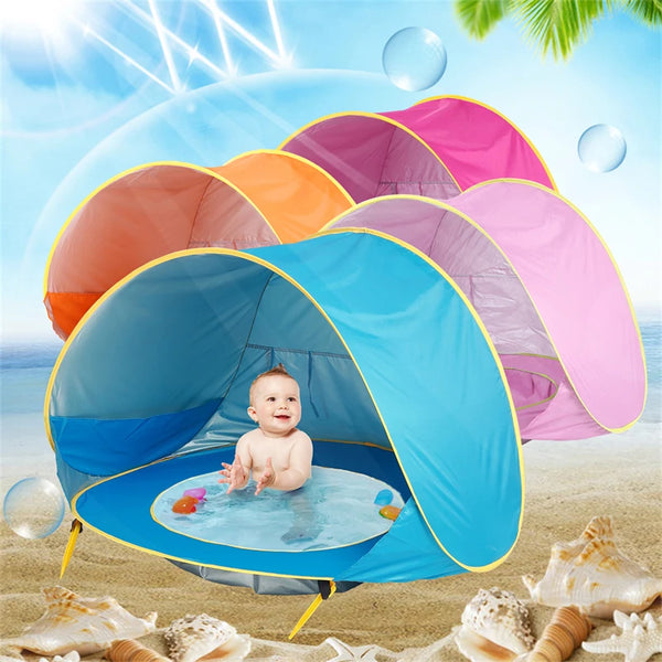 A portable baby beach tent is open on the sand, with a baby inside and water balls floating around.