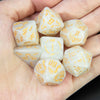 A set of white marble polyhedral dice featuring an orange gold dragon pattern held in a person's hand.