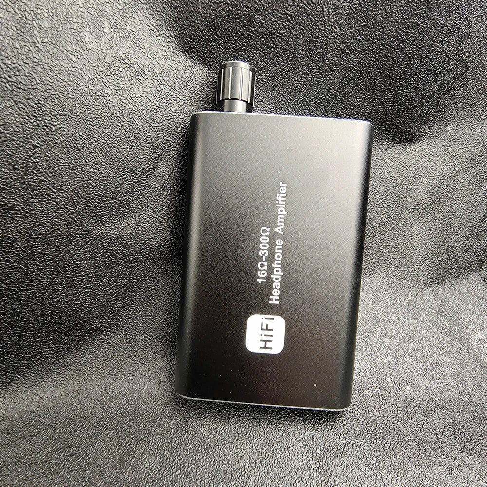 A black portable HiFi headphone amplifier with a silver cap is shown against a dark gray textured background.