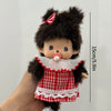 A small brown plush cartoon character with black fur, a red and white checkered outfit, and a striped bow.