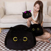 A woman is holding a black cat plush toy in her hand while sitting on a sofa with a checkered rug.