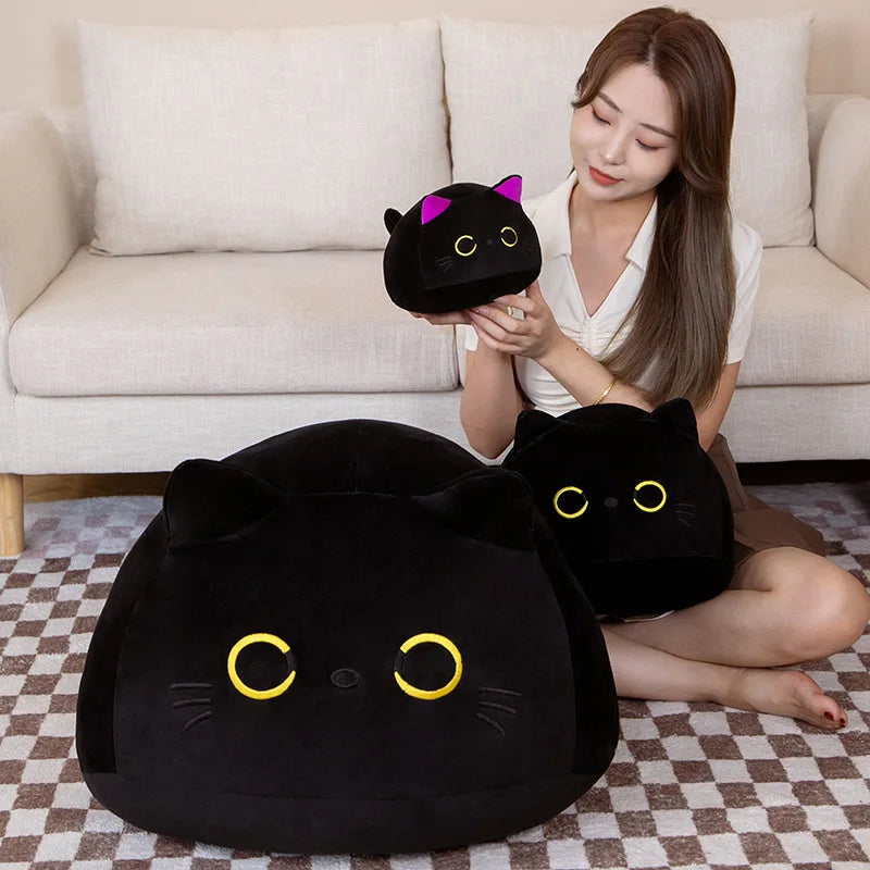 A woman is holding a black cat plush toy in her hand while sitting on a sofa with a checkered rug.