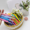 A hand holds an ergonomic crochet hook set with stitch markers and needles, featuring various colors like pink, blue, yellow,