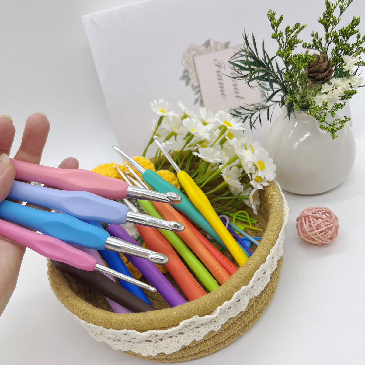 A hand holds an ergonomic crochet hook set with stitch markers and needles, featuring various colors like pink, blue, yellow,