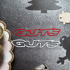 A close-up of red and silver vinyl stickers spelling GUTS on a dark surface.