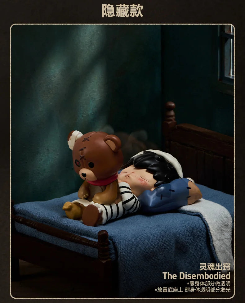 A brown bear collectible figure with a red collar is resting on a blue fabric, next to a white-covered figure.