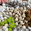 A close-up of various handcrafted crochet animal keychains in shades of white, gray, brown, and lime green.