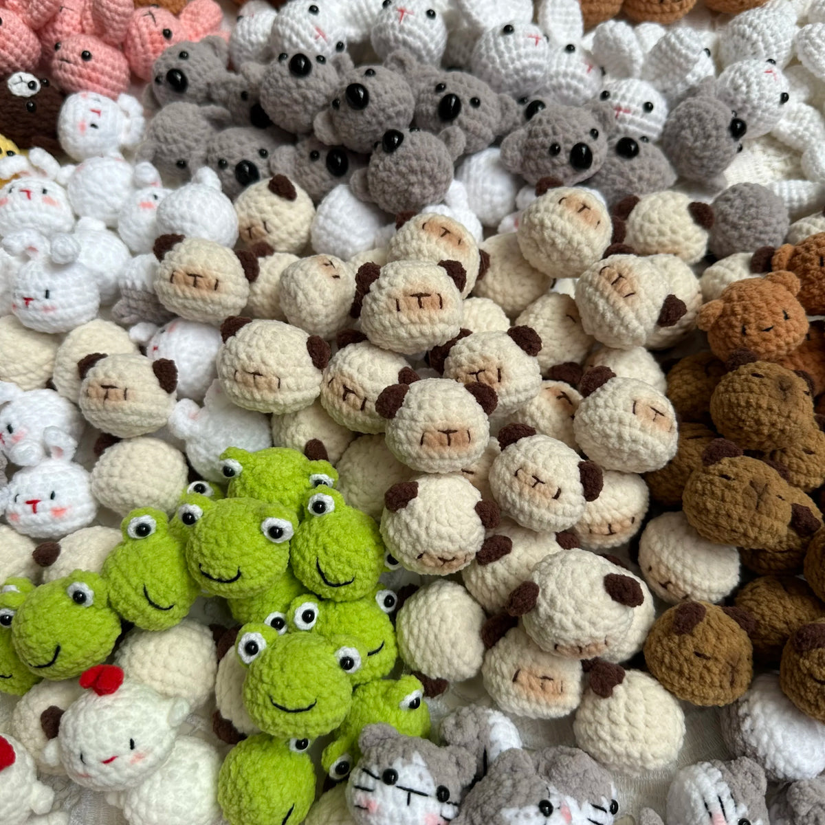 A close-up of various handcrafted crochet animal keychains in shades of white, gray, brown, and lime green.