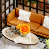 A miniature dollhouse puzzle kit displayed on a wooden table with an orange rose and white fluffy cushion.