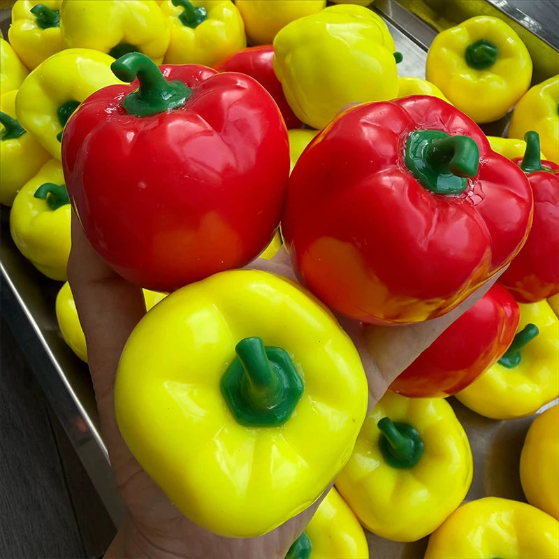 A hand holds a bright red bell pepper fidget toy surrounded by yellow bell peppers.