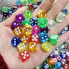 A hand holds a collection of colorful transparent dice in various shades of green, purple, yellow, and blue.