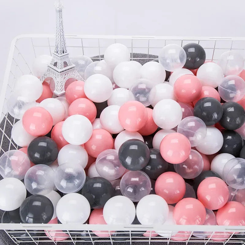 A white basket filled with a variety of colorful clear and opaque play balls in pink, white, and black.