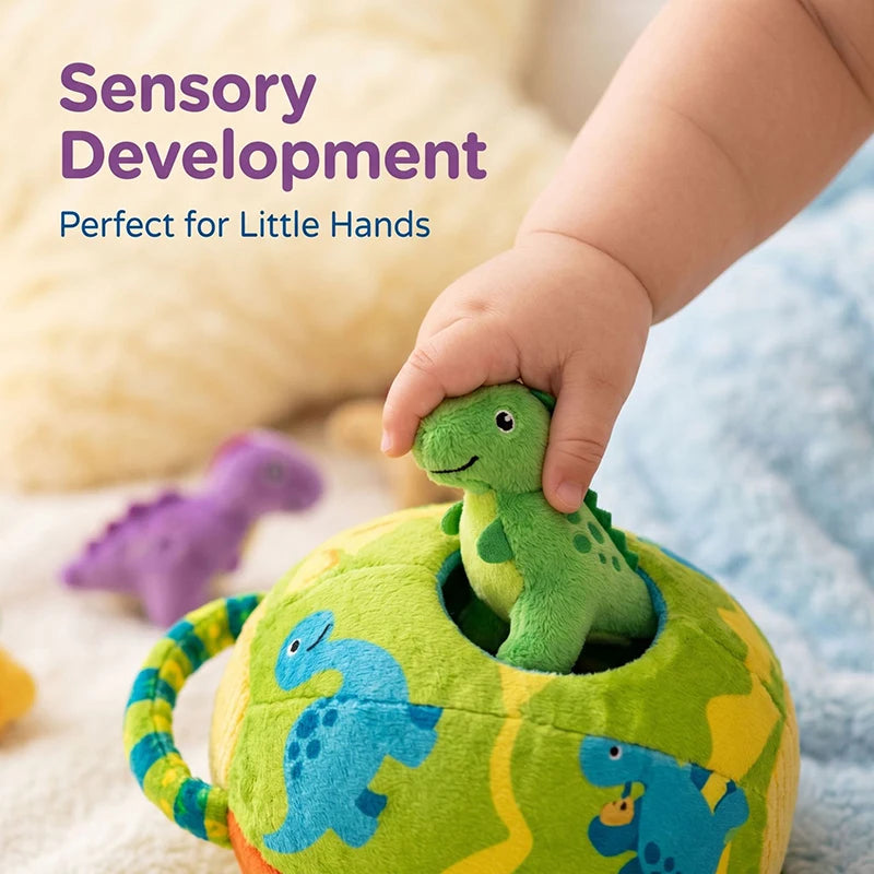 A baby's hand is placing a green dinosaur plush toy into an open, colorful plush sorting toy.