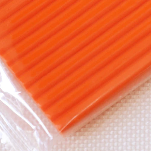 A close-up view of bright orange polymer clay modeling material packaged in clear plastic.