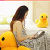 A woman is sitting on a bed with a yellow duck plush toy, looking at a tablet.