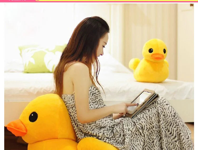A woman is sitting on a bed with a yellow duck plush toy, looking at a tablet.