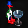 A red and blue classic drinking bird toy with a green feather is displayed next to a glass on a black background.