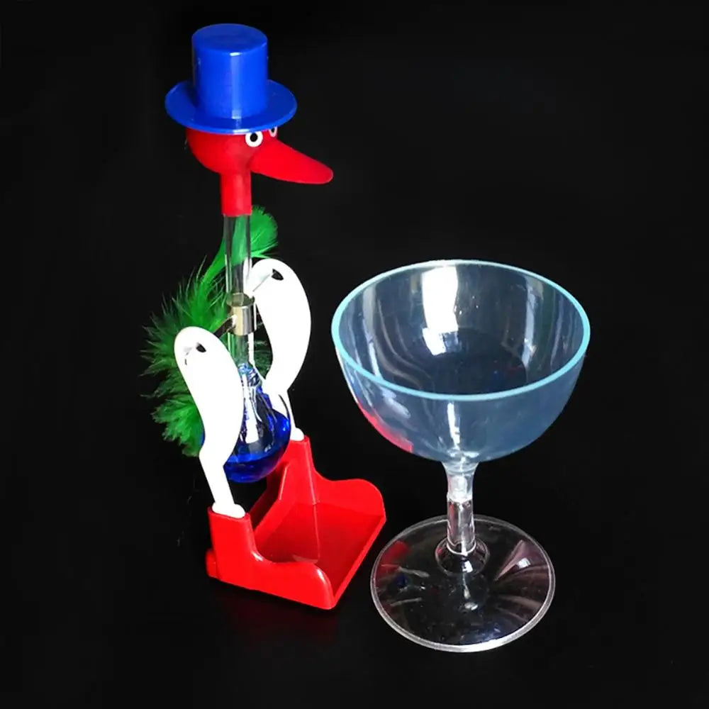 A red and blue classic drinking bird toy with a green feather is displayed next to a glass on a black background.