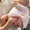 A person is holding a realistic reborn baby doll with a cloth body in a white knitted sweater.