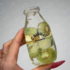 A hand holds a clear glass bottle filled with sliced kiwi fruit, used as a drink cup toy.