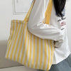 Sac cabas à épaule en toile rayée jaune et blanc porté par une personne en chemise blanche à manches longues.