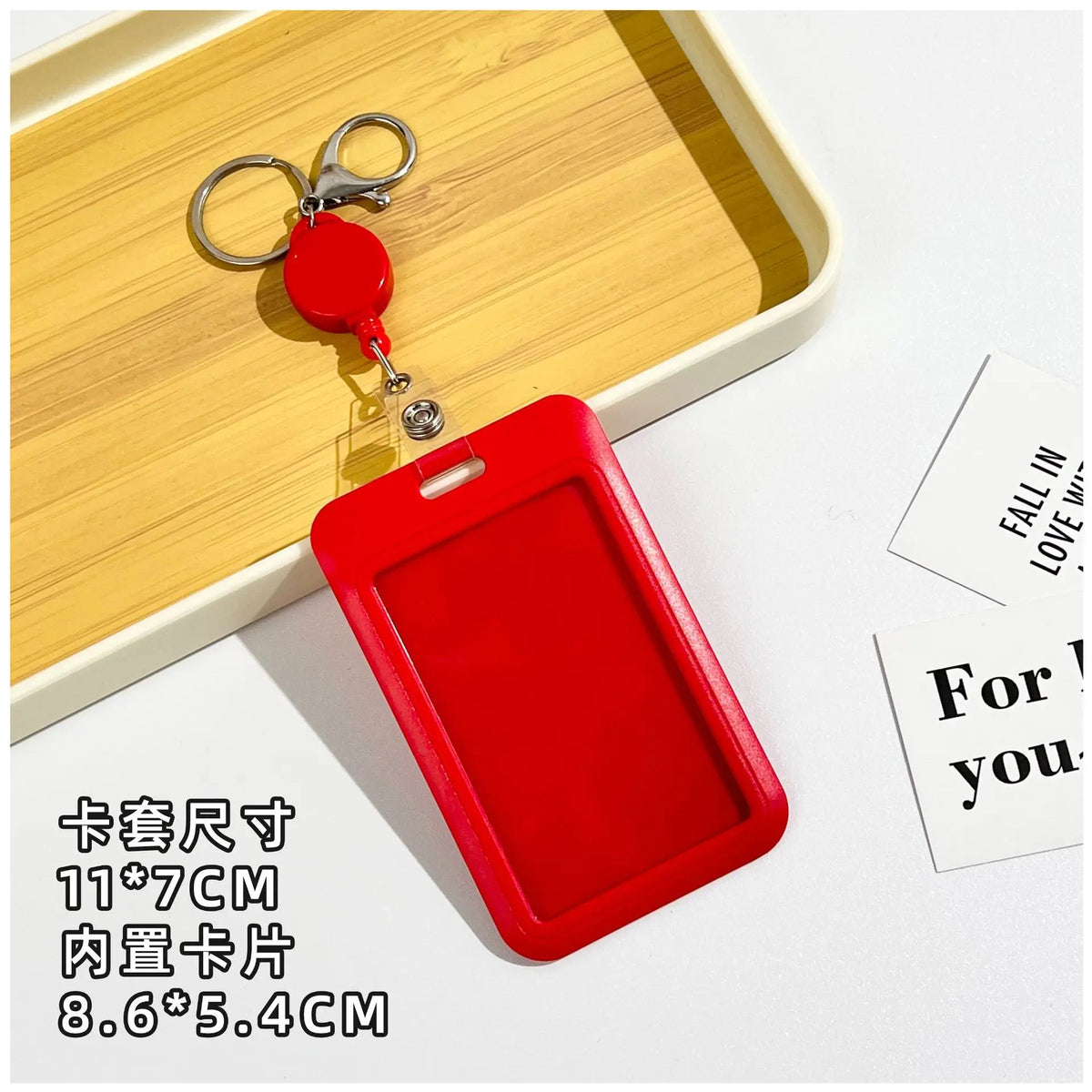 A red retractable ID badge holder with a clip is shown resting on a wooden tray.