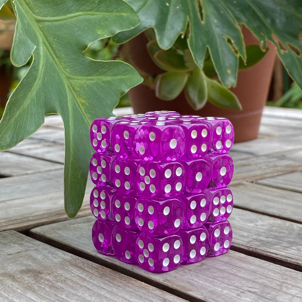 A stack of 36 transparent colorful dice in a clear display case resting on a wooden surface.