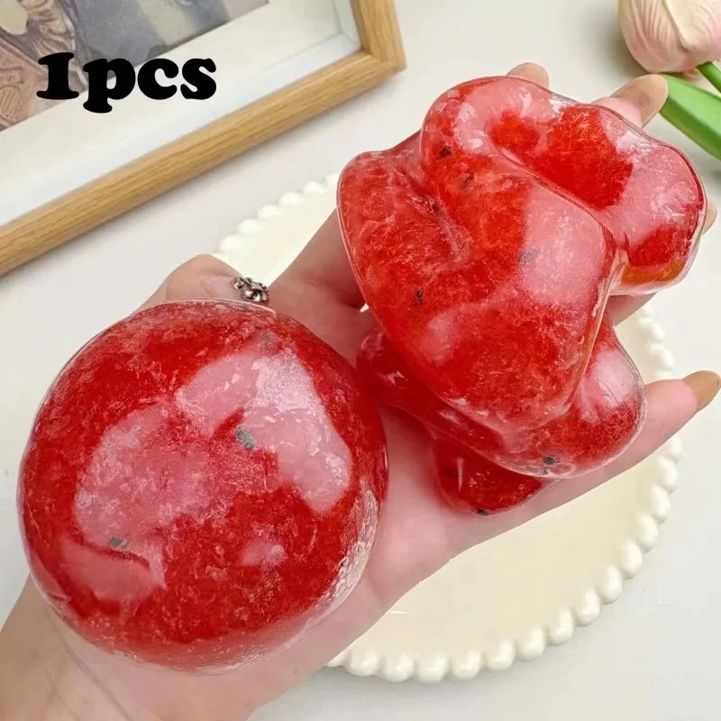 A hand holds several bright red, squishy stress relief toys shaped like strawberries.