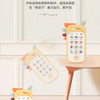 A yellow baby phone toy with colorful buttons is displayed on a wooden table, surrounded by decorative leaves.