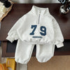 A light gray kids' 2-piece long-sleeve sweater and sweatpants set featuring a large navy blue number 79 on the chest.