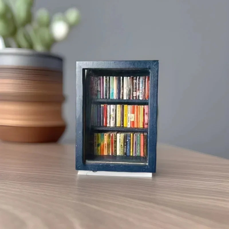 A dark blue wooden miniature bookshelf ornament filled with colorful books sits on a wooden surface.