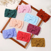 A collection of colorful nylon knit bow headbands for baby girls arranged in a wooden frame.