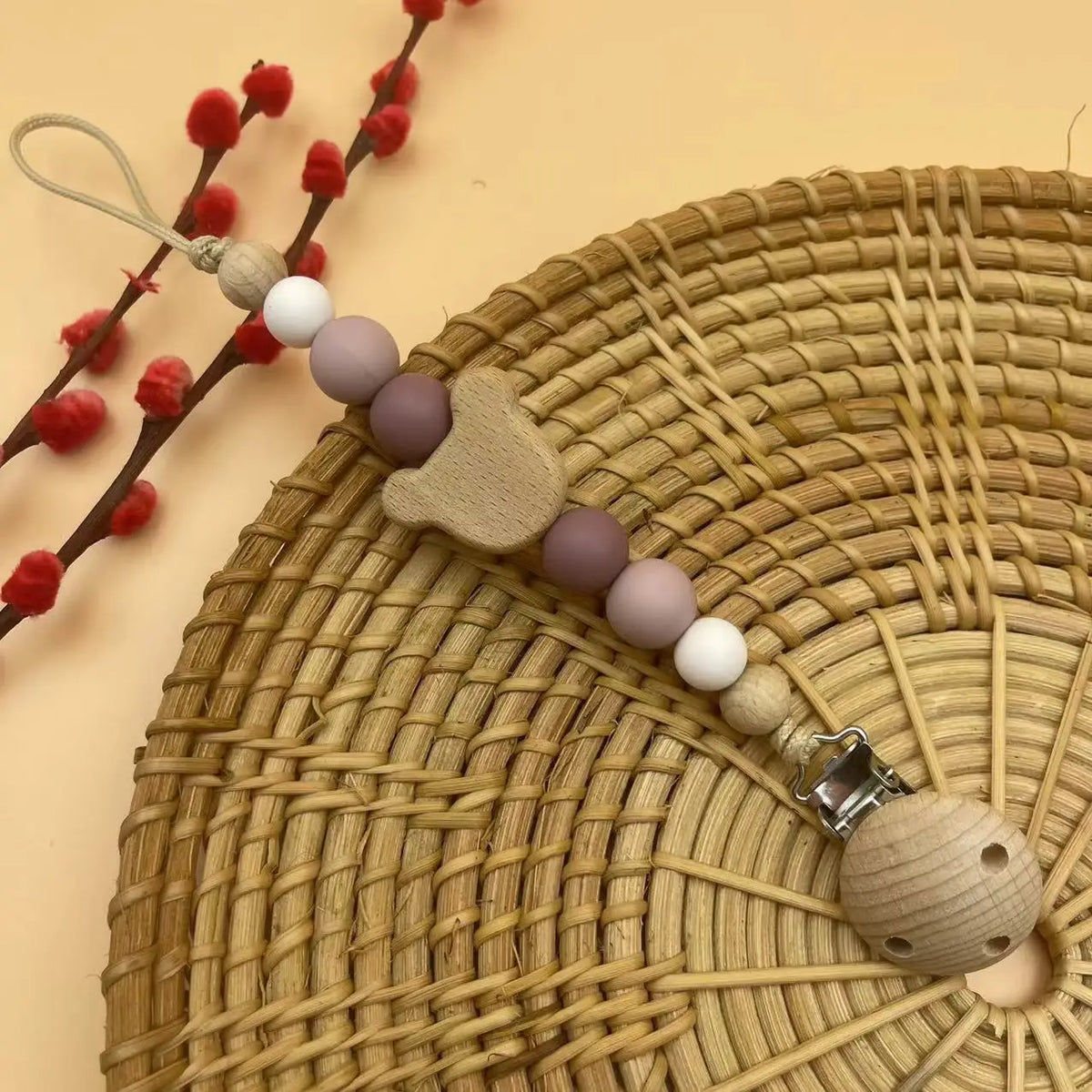 A wooden baby pacifier clip featuring silicone beads and a natural wood piece, resting on a woven mat.