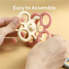 Hands assembling a silicone teether set for babies consisting of three pink and white rattle chew toys.