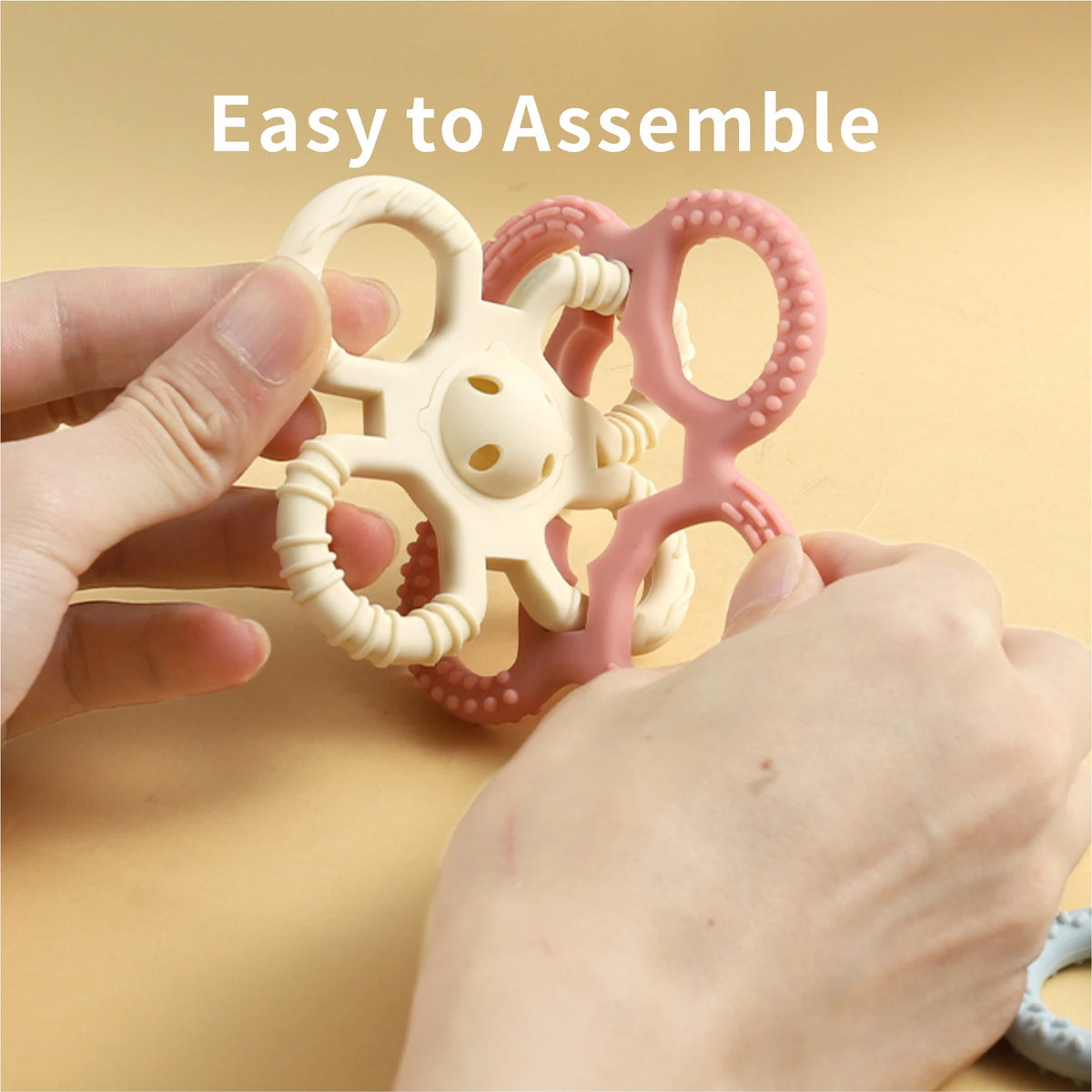 Hands assembling a silicone teether set for babies consisting of three pink and white rattle chew toys.