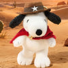 A white plush figurine of a dog wearing a brown cowboy hat and a red bandana in a desert landscape.