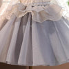 A light gray tulle dress for girls featuring ruffled layers and a pearl-encrusted waistband.